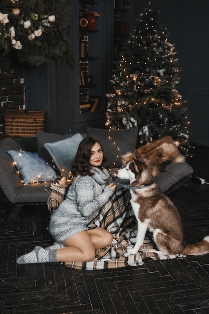 La donna è seduta con husky vicino al divano e all'albero di natale.