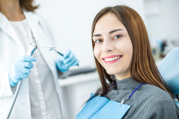 Una donna sta sorridendo con i denti bianchi e sani mentre si siede in una sedia dentale. medico dentista e paziente felice.