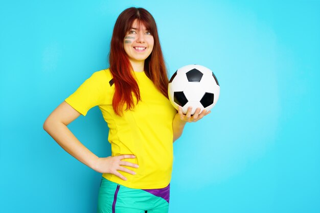 Woman is socccer fan in yellow t-shirt with soccer ball on blue background