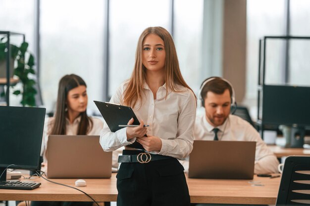 La donna è in piedi di fronte ai suoi colleghi uomini d'affari in abiti formali stanno lavorando in ufficio insieme