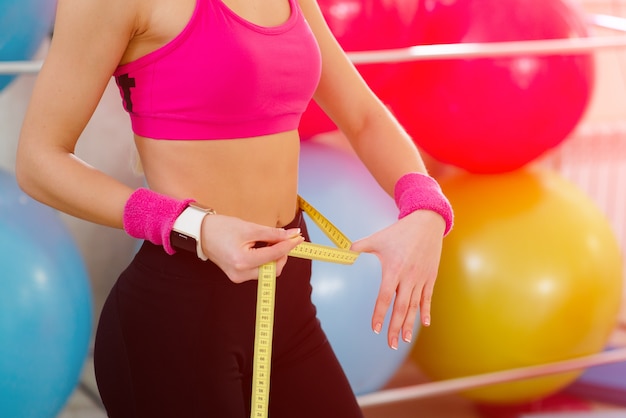 Photo the woman is standing and measuring her waist with a tape-line