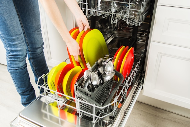 Woman is standing near dishwasher and taking clean plate from it