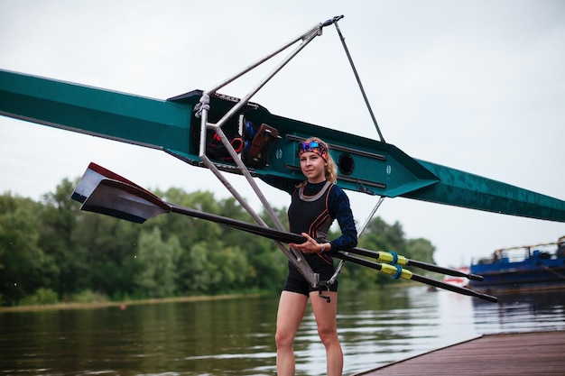 Woman is standing posing handling a kayak and laughing on the river bank