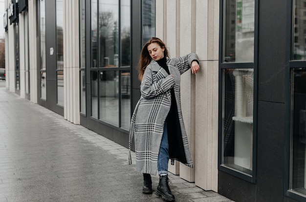 A woman is standing on the sidewalk in front of a house in a gray coat