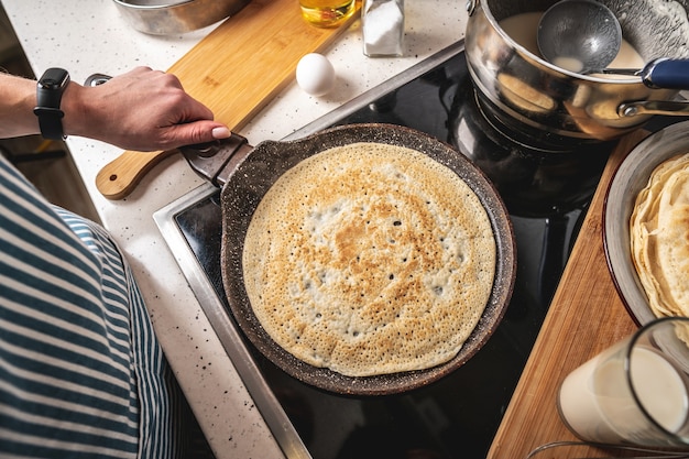 女性はストーブに立って、熱い鍋でパンケーキを揚げています