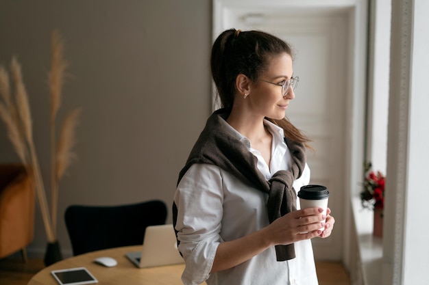 Una donna sta facendo una pausa in ufficio con in mano un bicchiere di caffè