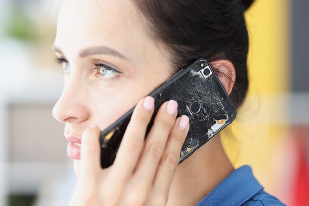 Женщина говорит на сломанном черном смартфоне концепции ремонта мобильного оборудования