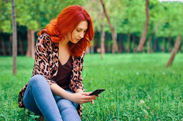 Woman is texting messages while sitting on the grass.