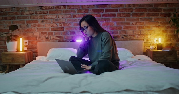 A woman is using a laptop while sitting on the bed