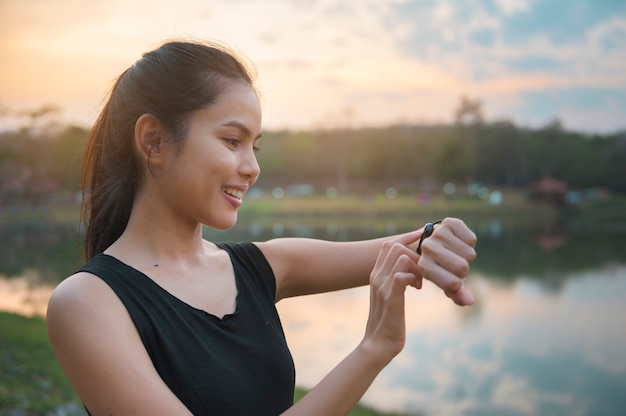 女性は日没時に屋外の自然の中で運動しながらスマートウォッチを使用しています