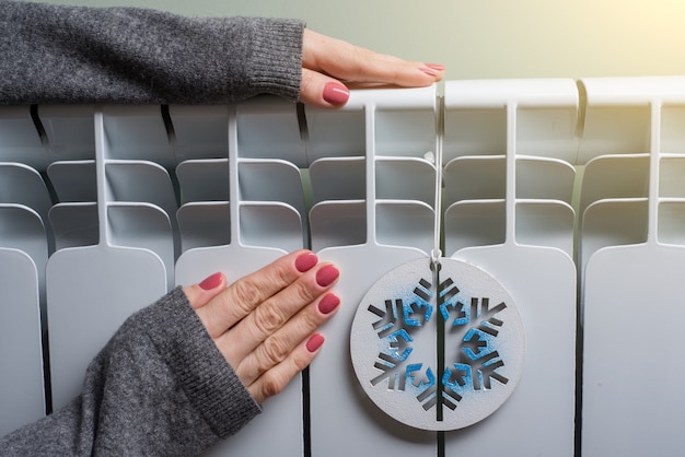 Photo woman is warming her hands on the radiator panel