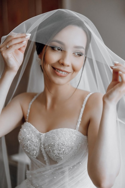 A woman is wearing a white wedding dress and holding a veil over her face