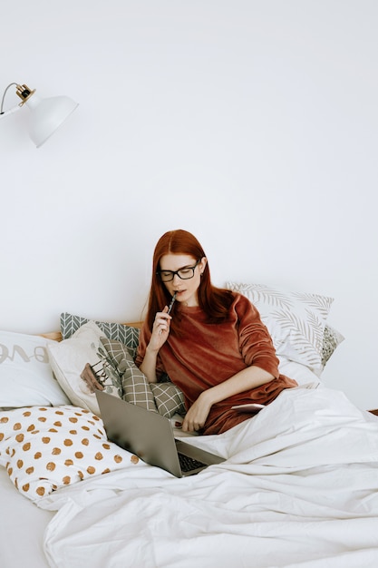 A woman is working on a laptop in her bedroom at home