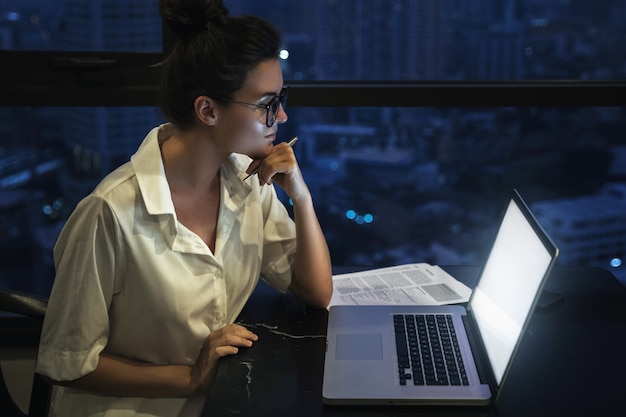 La donna sta lavorando con il computer portatile a casa durante la notte.