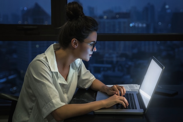 Woman is working with laptop at home during night.