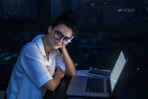 Woman is working with laptop at home during night.