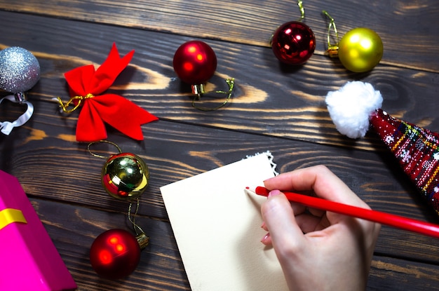 Woman is writing Christmas postcards. Greetings with holidays. Happy new year time. Congratulations to friends and family. Decorations on wooden table. Cozy mood. Copy space place.