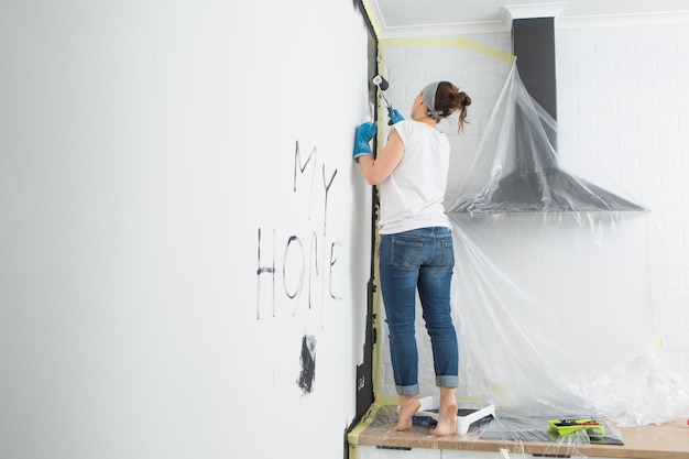 女性は私の家の壁に書いています女性は黒いペンキで壁を塗っています