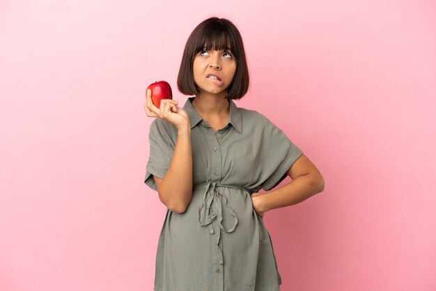 Donna su sfondo isolato incinta e frustrata mentre tiene in mano una mela