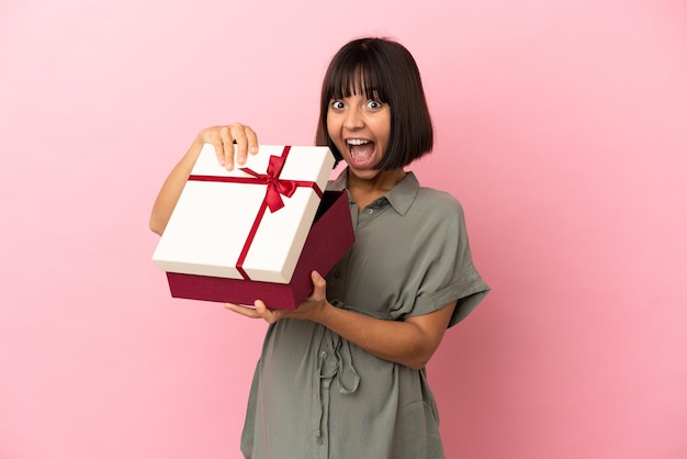 Woman over isolated background pregnant and holding a gift with surprised expression