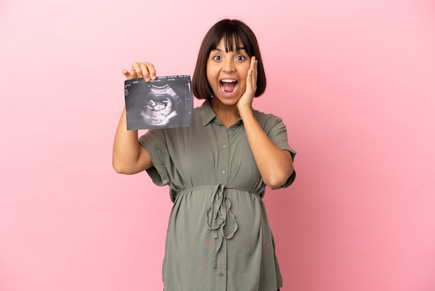 Woman over isolated background pregnant and surprised while holding an ultrasound