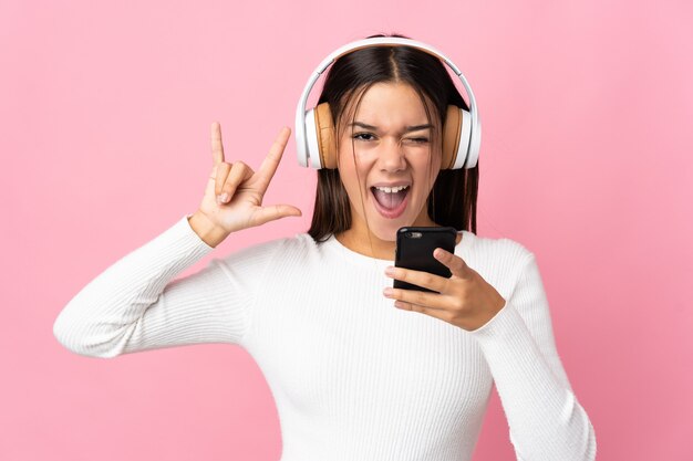 woman isolated on blue listening music with a mobile making rock gesture