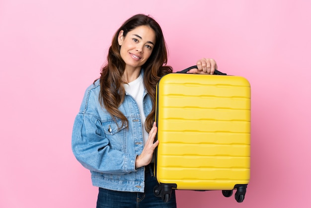 Woman over isolated blue in vacation with travel suitcase