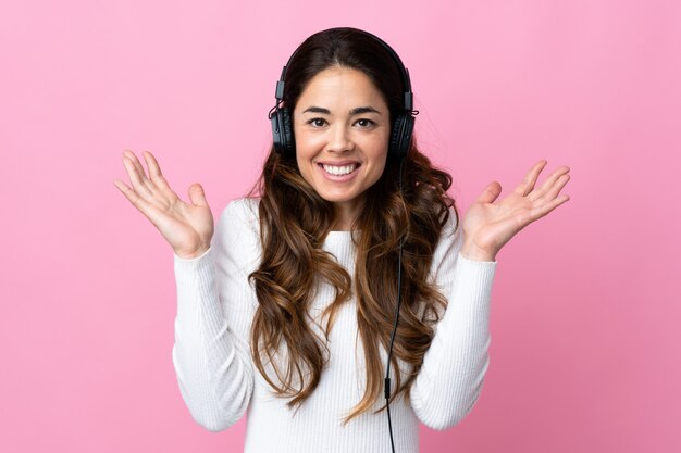 Woman over isolated pink surprised and listening music