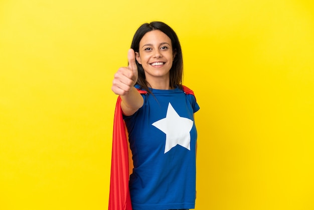 Woman isolated on yellow background in superhero costume with thumb up