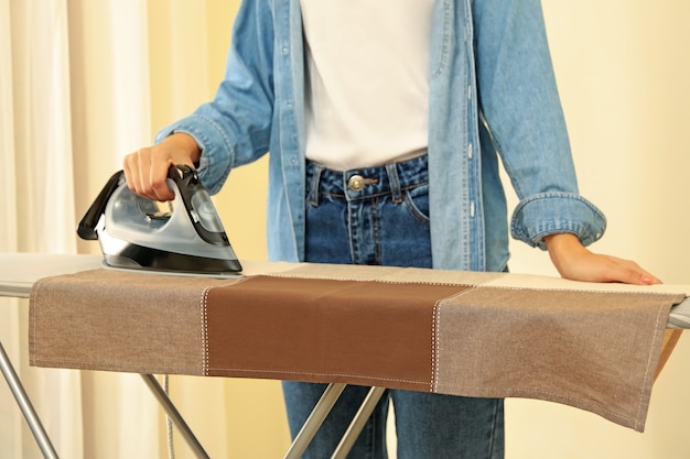 Woman in jeans ironing kitchen towel on ironing board