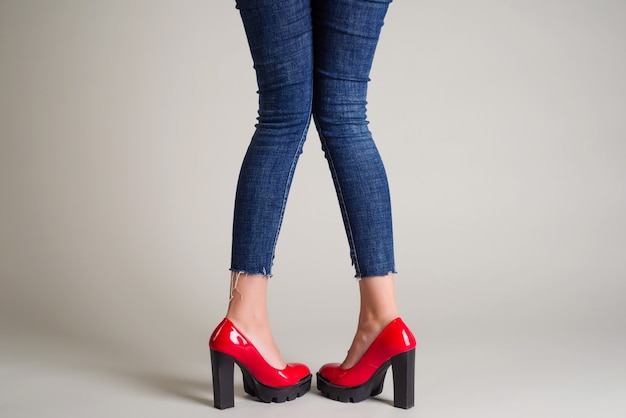 Woman in jeans red shoes with black heels posing on gray