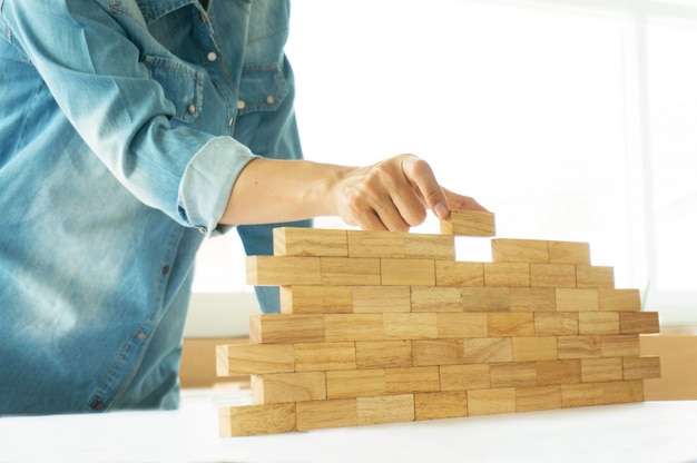 Foto donna in camicia jeans blocchi di blocco gioco di legno (jenga) costruzione di un piccolo muro di mattoni concetto di rischio