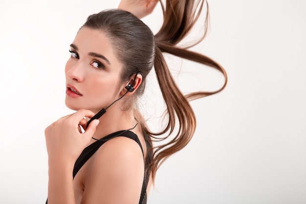 woman in jogging black top listening to music on earphones posing isolated on white