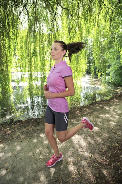 Foto donna che fa jogging sul sentiero vicino alle piante nel parco