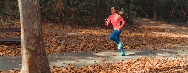 写真 秋に公園の歩道でジョギングをしている女性