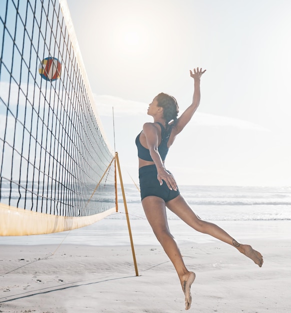 Woman jump and volleyball on beach by net in serious sports match game or competition Body of female person jumping for ball in volley for spike fitness or healthy wellness in exercise by ocean