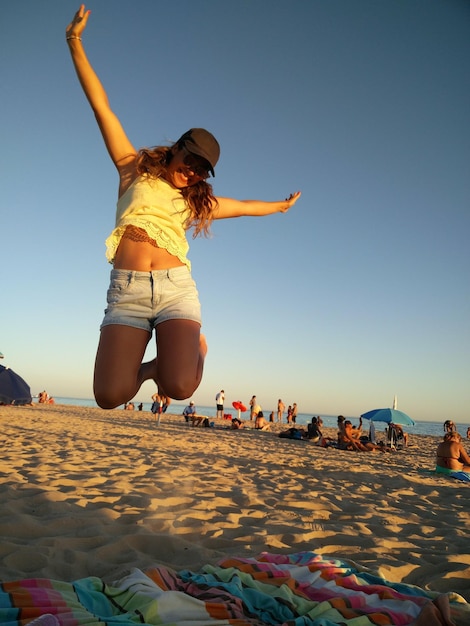 晴れた空の前でビーチでジャンプする女性