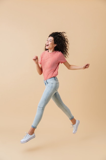 Woman jumping isolated over beige wall.