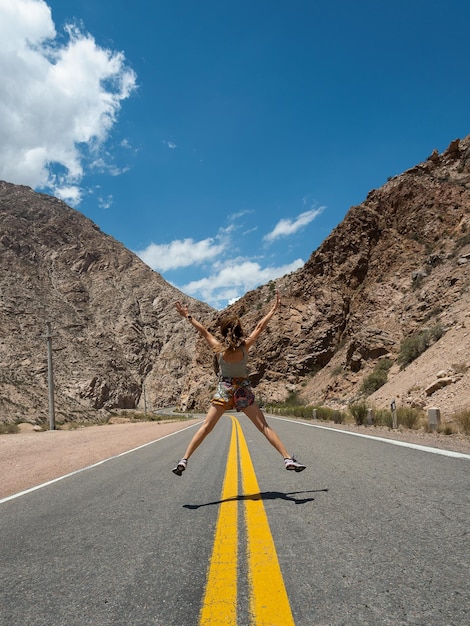 아르헨티나 멘도사에서 산이 있는 빈 도로에서 기쁨을 위해 점프하는 여성
