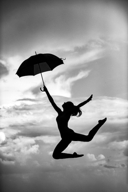 Женщина прыгает с танцором балета под зонтиком на фоне неба.