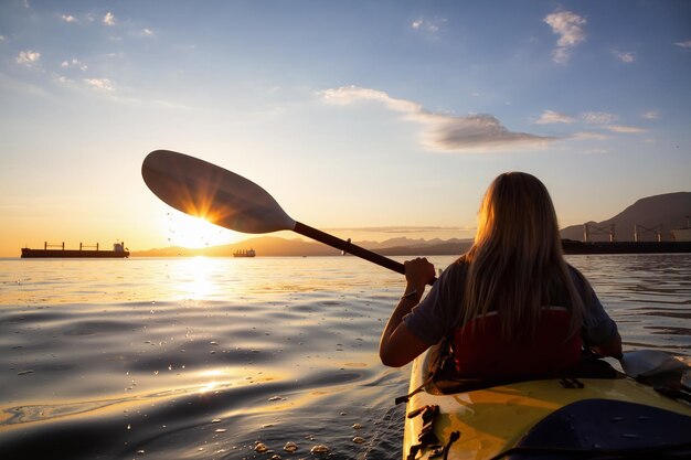 Woman on a kayak is paddeling in the ocean during a vibrant sunset