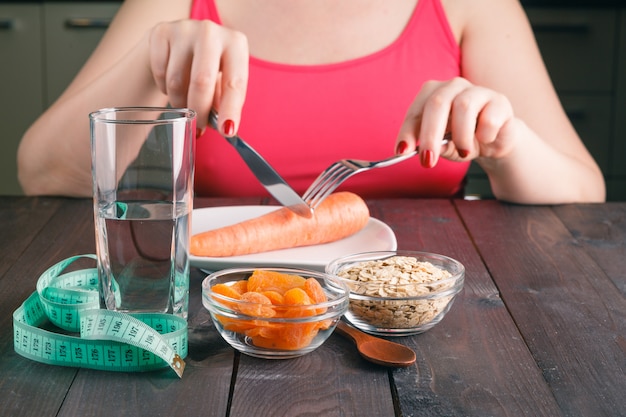 Woman keeping a diet and eating carrot in the kitchen