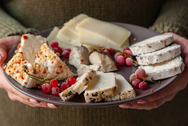 Woman keeps in her hands dark ceramic plate with assorted goat farmer cheese