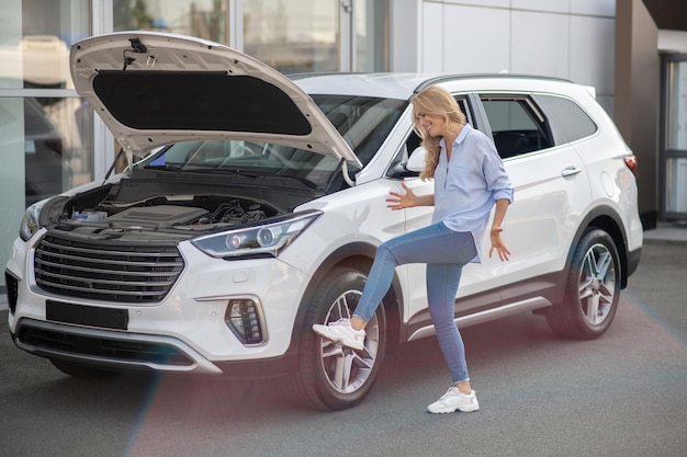 Woman kicking tire of car standing with hood open