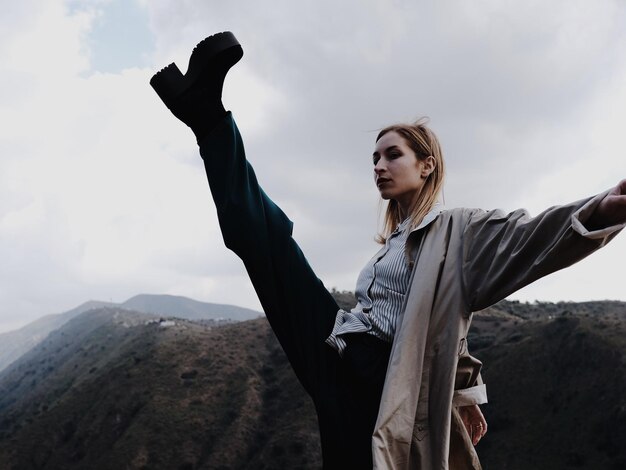 Foto donna che calcia mentre è in piedi sulla montagna contro il cielo