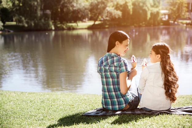 Woman and kid are sitting at the edge of water and looking at each other