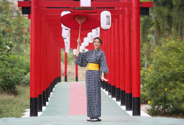 Una donna in kimono con in mano un ombrello che entra nel santuario, nel giardino giapponese.