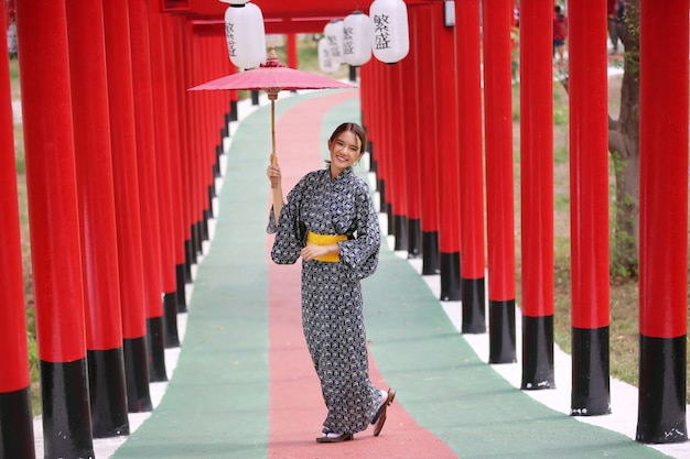 日本庭園の神社に傘をさして歩いている着物姿の女性。