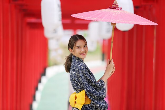 A woman in kimono holding umbrella walking into at the shrine, in Japanese garden.