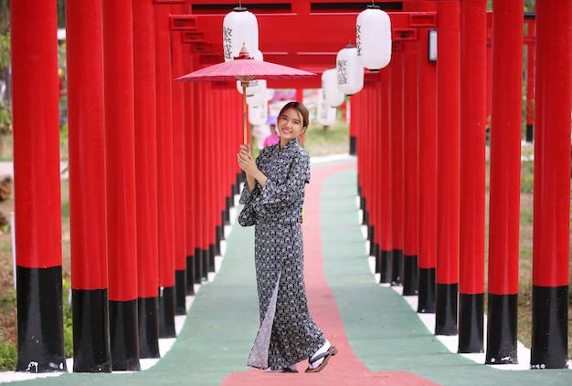 A woman in kimono holding umbrella walking into at the shrine, in Japanese garden.